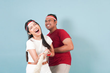 Two couple Indonesian wearing flag headband are pulling on a rope, joining competition for Indonesian Independence Day. Scene is lighthearted and fun.の写真素材
