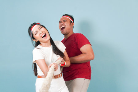 Two couple Indonesian wearing flag headband are pulling on a rope, joining competition for Indonesian Independence Day. Scene is lighthearted and fun.の写真素材