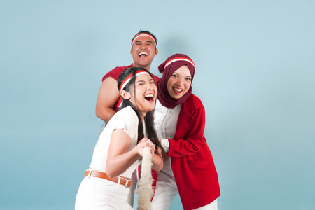 Three people cheerful Indonesian wearing flag headband are pulling on a rope, joining competition for Indonesian Independence Day. fun gameの写真素材
