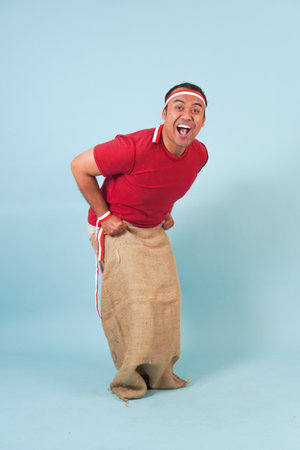 Young Indonesian man wearing gunny sack joining a competition, getting ready to jump in a sack....