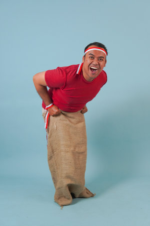 Young Indonesian man wearing gunny sack joining a competition, getting ready to jump in a sack....
