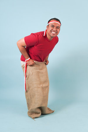 Young Indonesian man wearing gunny sack joining a competition, getting ready to jump in a sack. Indonesia Independence Day concept. traditional gameの写真素材