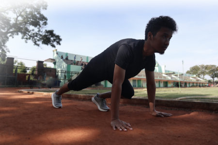 Young asian runner ready to running in the start position on dirt field. The man is wearing a grey...