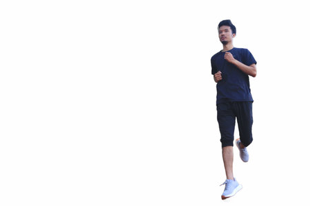 A man is running in a park with a fence in the background. The man is wearing a blue shirt and black shortsの写真素材