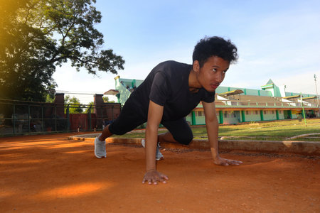 Young asian runner ready to run in the start position on dirt field. The man is wearing a black...