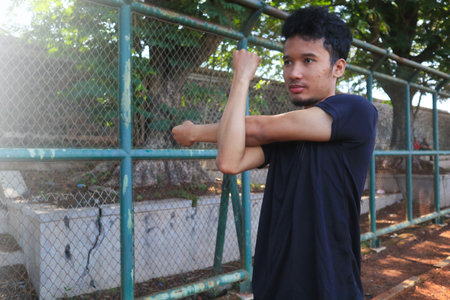 A man is stretching his arm in front of a fence. Concept of determination and focus as the man works on his flexibilityの写真素材
