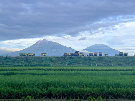 A mountain range is in the background with a field of green grass in front. There are many trucks on...