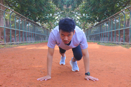 Young asian runner ready to running in the start position on dirt field. The man is wearing a grey...