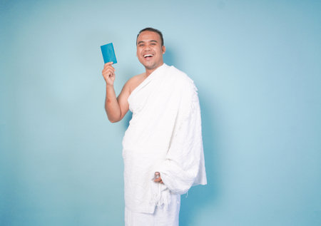 young Asian Muslim man wearing ihram posing pose while holding passpor isolated blue background. Hajj concept. islamの写真素材
