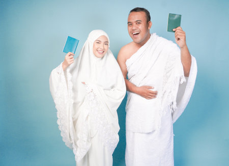 young Asian Muslim couple in ihram and prayer gown posing with a passport over isolated by blue background. Hajj concept. cople islam muslim conceptの写真素材
