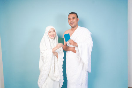 young Asian Muslim couple in ihram and prayer gown posing with a passport over isolated by blue background. Hajj concept. cople islam muslim conceptの写真素材