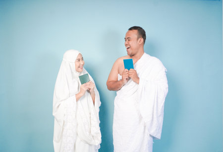 young Asian Muslim couple in ihram and prayer gown posing with a passport over isolated by blue background. Hajj concept. cople islam muslim conceptの写真素材