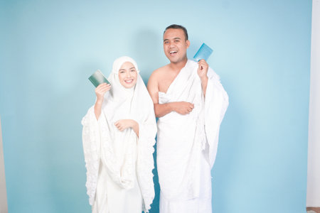 young Asian Muslim couple in ihram and prayer gown posing with a passport over isolated by blue background. Hajj concept. cople islam muslim conceptの写真素材