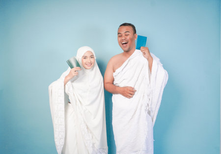 young Asian Muslim couple in ihram and prayer gown posing with a passport over isolated by blue background. Hajj concept. cople islam muslim conceptの写真素材