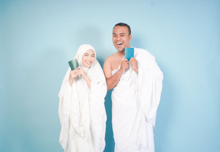 young Asian Muslim couple in ihram and prayer gown posing with a passport over isolated by blue background. Hajj concept. cople islam muslim conceptの写真素材