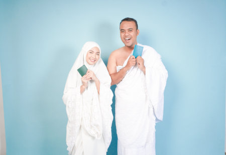 young Asian Muslim couple in ihram and prayer gown posing with a passport over isolated by blue background. Hajj concept. cople islam muslim conceptの写真素材