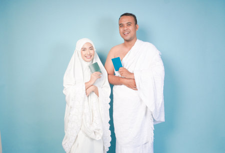 young Asian Muslim couple in ihram and prayer gown posing with a passport over isolated by blue background. Hajj concept. cople islam muslim conceptの写真素材