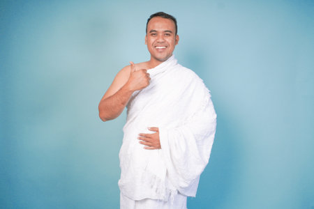 Excited Asian Muslim man wearing ihram gesture thumbs up pose, isolated blue background. Hajj concept. islam muslim conceptの写真素材