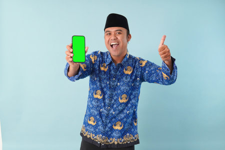 government worker man wearing kopri blue batik uniform He is is glasses pointing to copy space on his smartphone. PNS, ASN civil servant concept.の写真素材