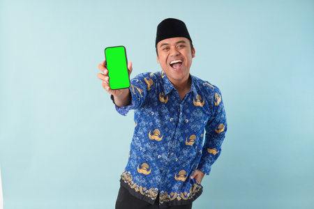 government worker man wearing kopri blue batik uniform He is is glasses pointing to copy space on his smartphone. PNS, ASN civil servant concept.の写真素材