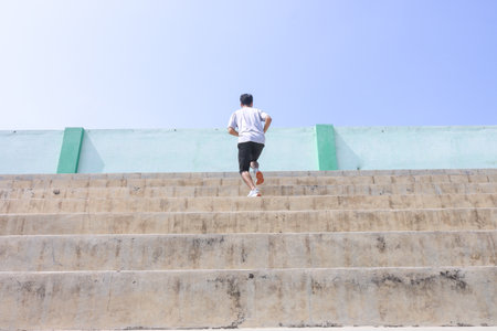 A man is running up a set of stairs. Concept of determination and perseverance as the man pushes himself to reach the top of the steps. The man's focused expressionの写真素材