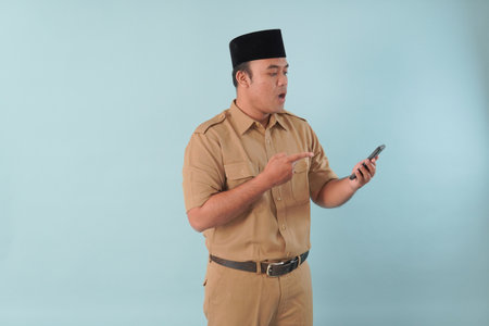 Smiling government worker with khaki uniform He is doing video call while pointing to his smartphone PNS, ASN civil servant concept.の写真素材