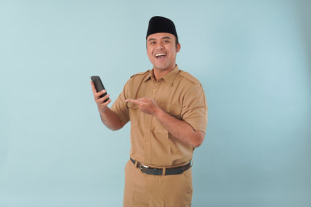 Smiling government worker with khaki uniform He is doing video call while pointing to his smartphone PNS, ASN civil servant concept.の写真素材