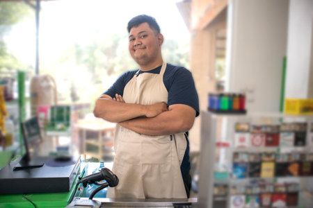 Smiling Asian young man as groceries or modermarket staff standing with crossed arms and full of confidence in front of display rackの写真素材
