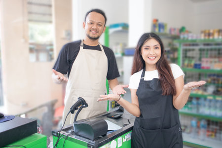 couple Friendly Asian cashier welcoming customer with open arms, cashier is wearing black and cream apron standing in a groceries or convenient storeの写真素材