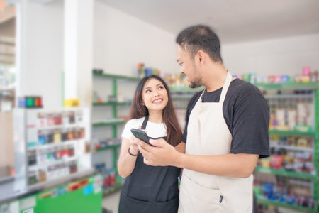 couple Confident young Asian people as convenience store or modern market staff in apron standing with pointing the phone while standing in front of display shelf.の写真素材