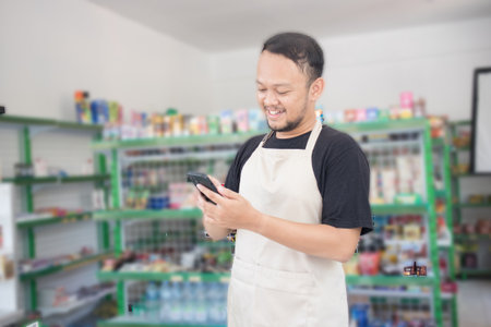 Asian male work as groceries store or modern market staff smiles and looks at the phone, wearing...
