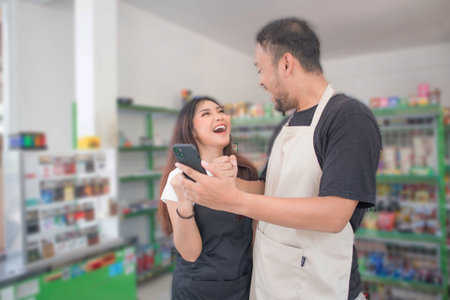 couple Confident young Asian people as convenience store or modern market staff in apron standing with pointing the phone while standing in front of display shelf.の写真素材