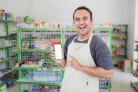 Asian male work as groceries store or modern store staff pointing to the copy space at smartphone...