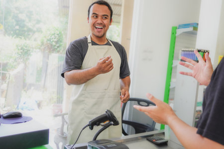 young asian man cashier worker standing near cashier counter in black apron and making payment and...