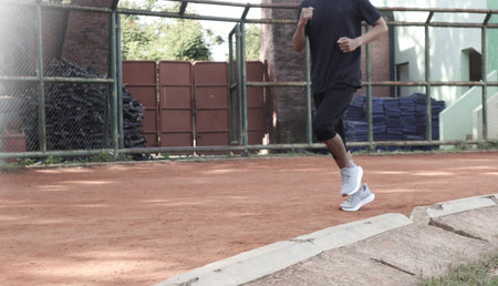 A man is running in a park with a fence in the background. The man is wearing a black shirt and...