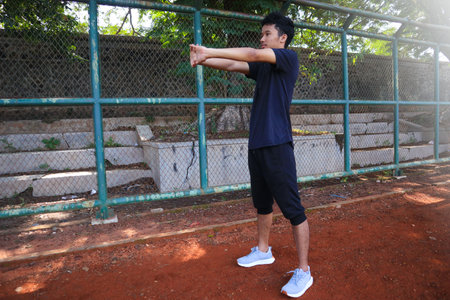 A man is stretching his arm in front of a fence. Concept of determination and focus as the man works...