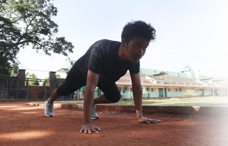 Young asian runner ready to running in the start position on dirt field. The man is wearing a grey...