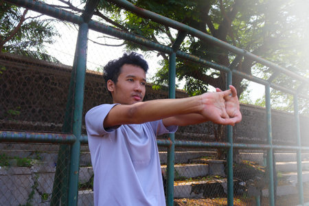 A man is stretching his arm in front of a fence. Concept of determination and focus as the man works...
