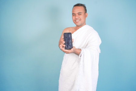 man muslim. Excited young Asian Muslim man wearing ihram presenting copy space on his smartphone...