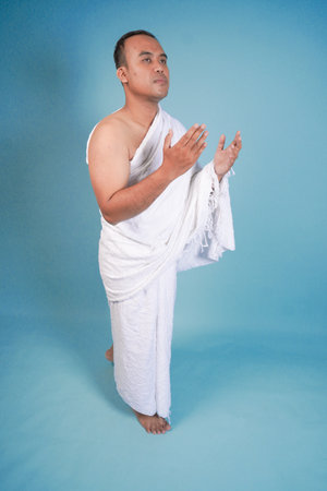 Young handsome Asian Muslim man wearing ihram walking while praying, performing tawaf isolated on...