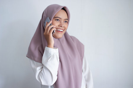 young muslim asian woman wearing a purple hijab a head scarf is talking on her cell phone. She is...