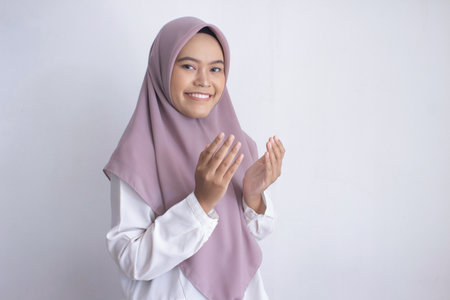 young muslim asian woman wearing a purple hijab, praying. The hijab is long and covers her head. She...