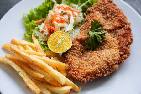 Chicken schnitzel is made from chicken breast, served with French fries, lemon, vegetable salad and...