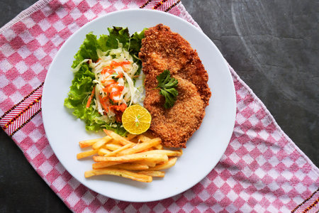 Chicken schnitzel is made from chicken breast, served with French fries, lemon, vegetable salad and...