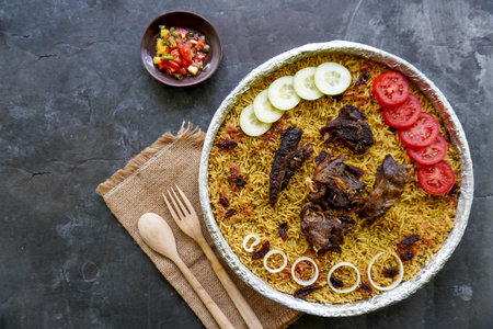 Traditional Kebuli Rice with Lamb, aromatic spiced rice dish cuisine, served with tender meat, raisins, cucumber, onion, seasoning and fresh tomato slicesの写真素材