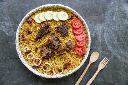 Traditional Kebuli Rice with Lamb, aromatic spiced rice dish cuisine, served with tender meat, raisins, cucumber, onion, seasoning and fresh tomato slicesの写真素材