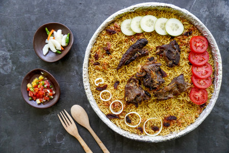 Traditional Kebuli Rice with Lamb, aromatic spiced rice dish cuisine, served with tender meat, raisins, cucumber, onion, seasoning and fresh tomato slicesの写真素材