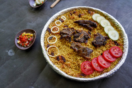 Traditional Kebuli Rice with Lamb, aromatic spiced rice dish cuisine, served with tender meat, raisins, cucumber, onion, seasoning and fresh tomato slicesの写真素材