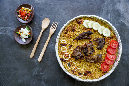 Traditional Kebuli Rice with Lamb, aromatic spiced rice dish cuisine, served with tender meat, raisins, cucumber, onion, seasoning and fresh tomato slicesの写真素材