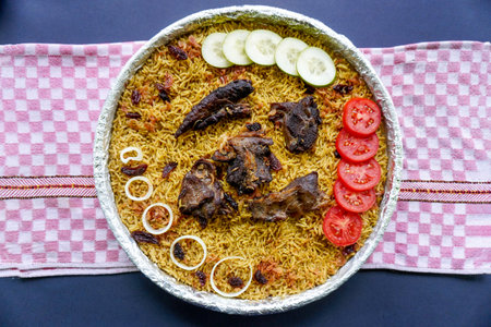Traditional Kebuli Rice with Lamb, aromatic spiced rice dish cuisine, served with tender meat, raisins, cucumber, onion, seasoning and fresh tomato slicesの写真素材